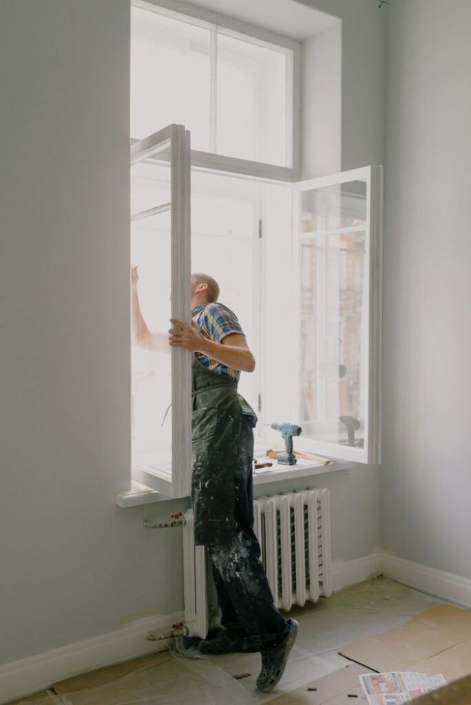 Side view of anonymous handyman in uniform mounting window frame during renovation process in flat
